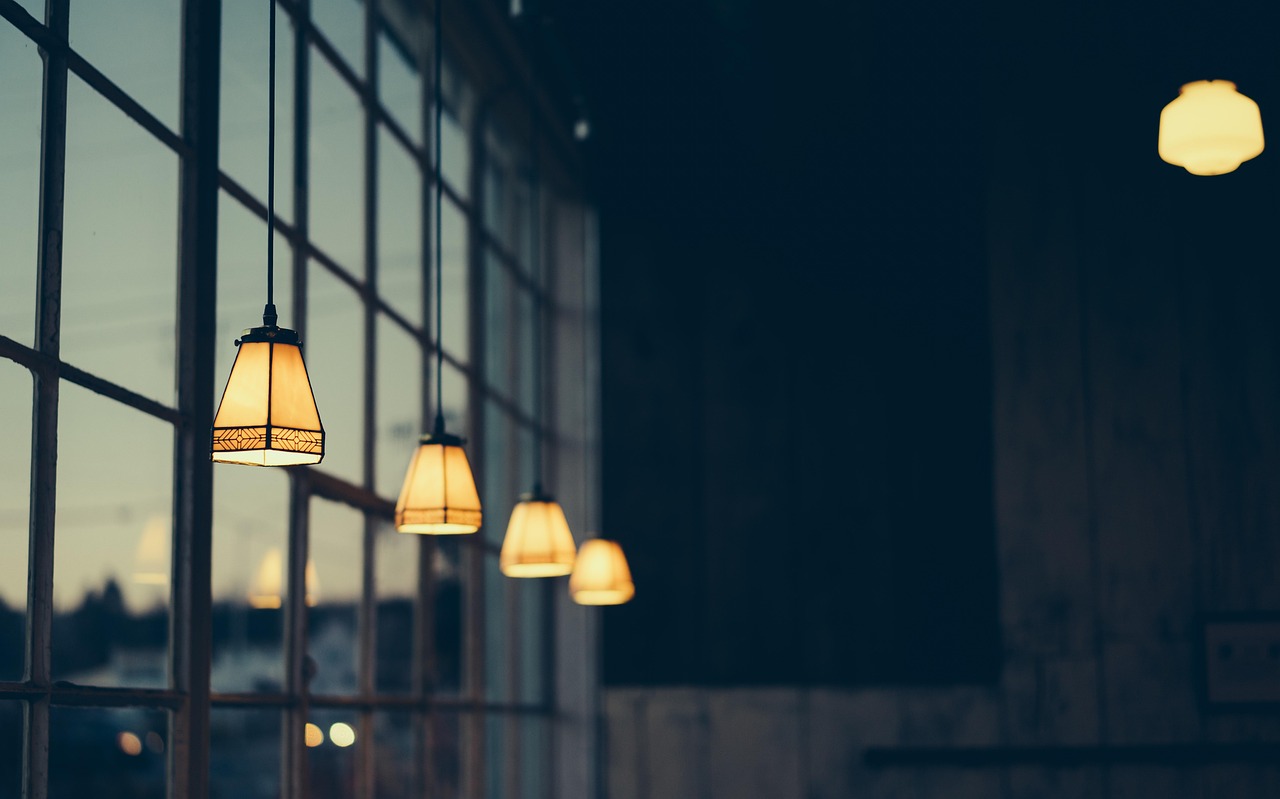 Lit pendant lamps hanging along a row of tall windows at dusk